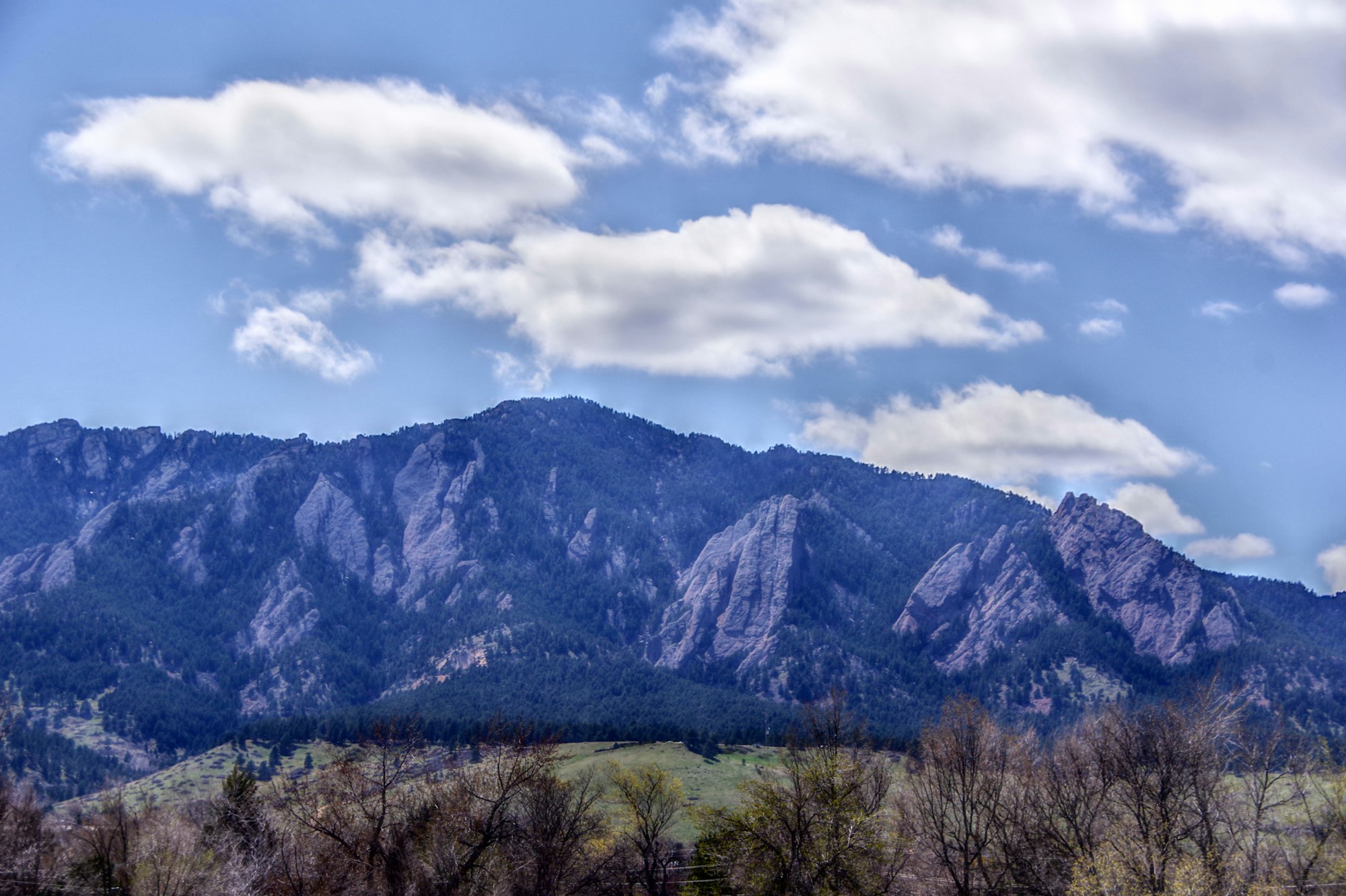 The Flatirons rock formations above Boulder, Colorado, seen across open ground under a blue sky