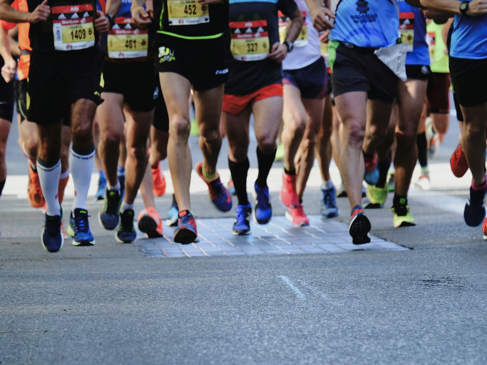 The legs of a packed field of road racers crossing a timing mat, race bibs visible
